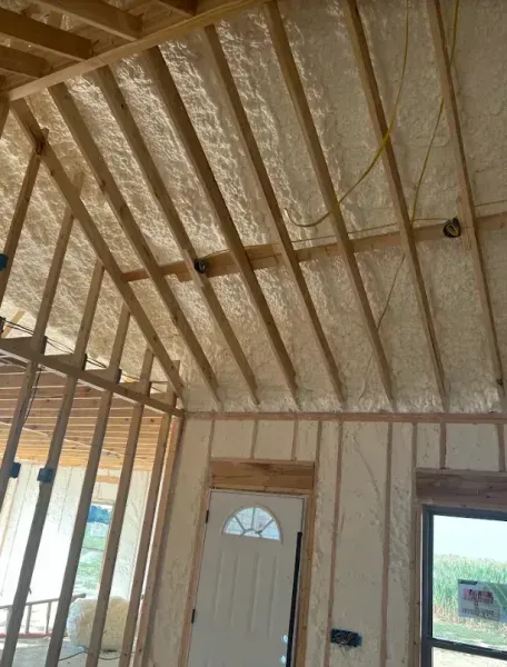 Interior of an unfinished room with wooden framing and walls insulated with spray foam.