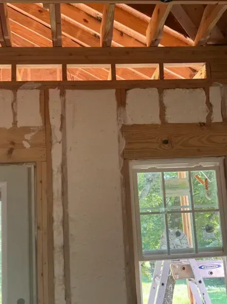 Interior wall framing during construction, showing exposed wooden studs, drywall patches, and an installed window.