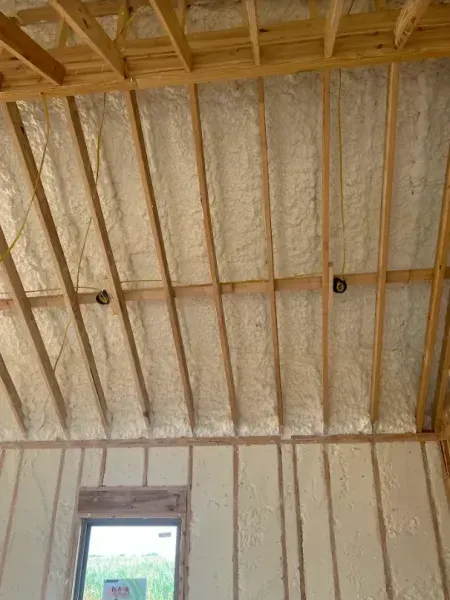 Interior view of a wood-framed room with unfinished walls and ceiling insulated with white spray foam.