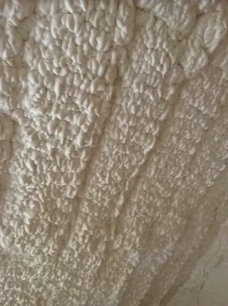 A close-up of a white, textured crochet blanket with repeating bumpy, ridged stitch patterns.