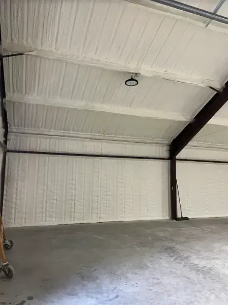 Interior of a warehouse with white spray-foam insulated walls and ceiling, metal support beams, and a concrete floor.