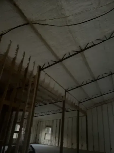 Interior of an unfinished room with metal framing, exposed ceiling trusses, and white spray foam insulation on walls.