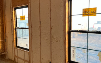 Two black-framed double-hung windows installed in an interior wall with exposed insulation and wooden framing studs.