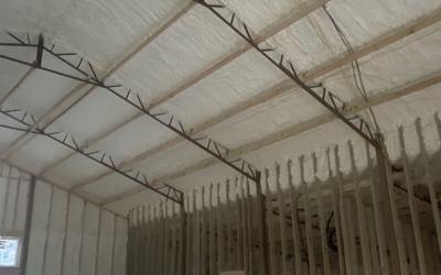 An unfinished building interior showing steel roof trusses and spray-foam insulation applied to the ceiling and walls.