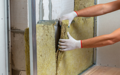 Hands in protective gloves installing mineral wool insulation panels into a metal wall frame.