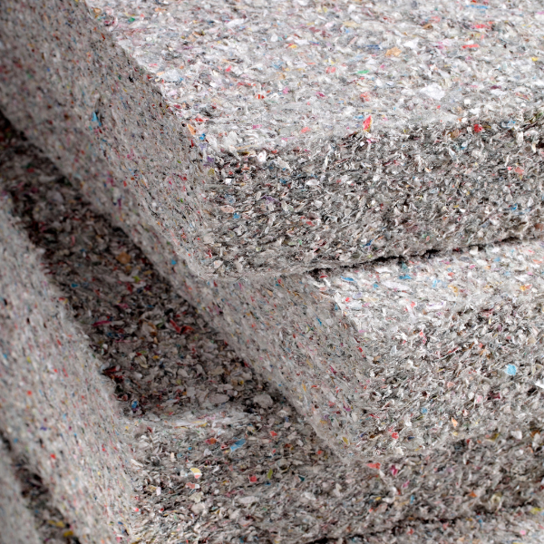 Stacked panels of dense, gray, fibrous recycled textile insulation material with small colorful flecks.
