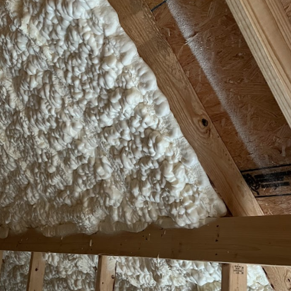 White spray foam insulation applied between wooden roof rafters and framing in an attic space.