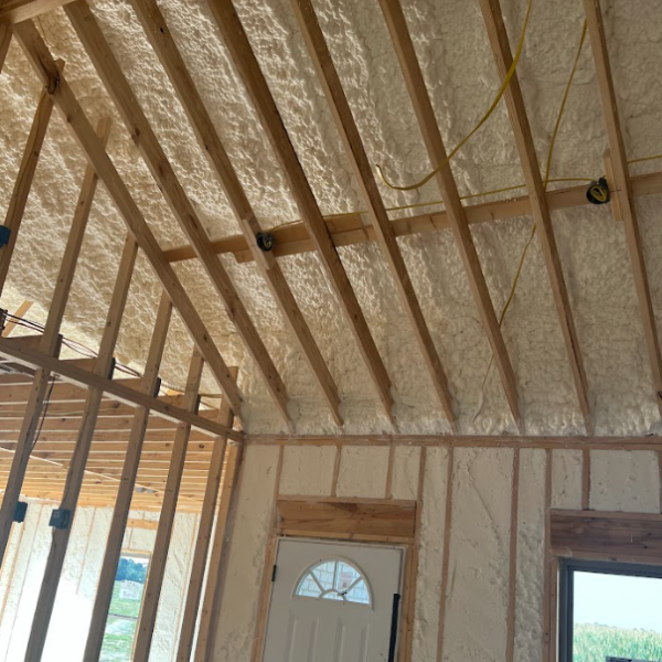 Interior of a building frame under construction with spray foam insulation applied between wooden ceiling and wall studs.