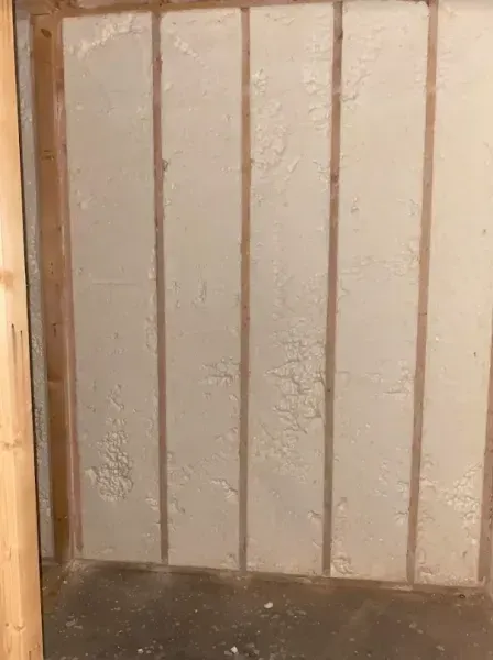A wood-framed interior wall with light-colored spray foam insulation between the studs.