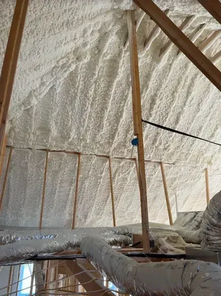 Attic interior showing spray foam insulation applied to the underside of the roof rafters and framing.
