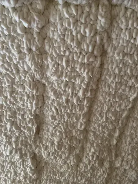 A close-up view of beige, uneven spray foam insulation with a textured, bumpy surface.