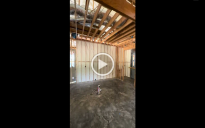 An interior view of a room under construction with exposed wooden framing, concrete flooring, and a central pipe.