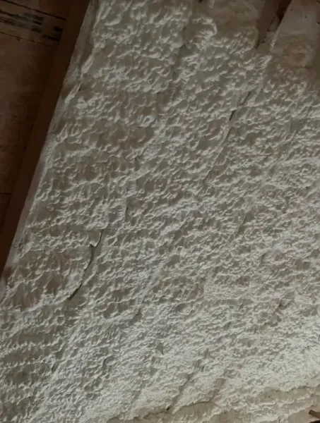Rough, white spray foam insulation applied to the underside of a wooden roof deck.