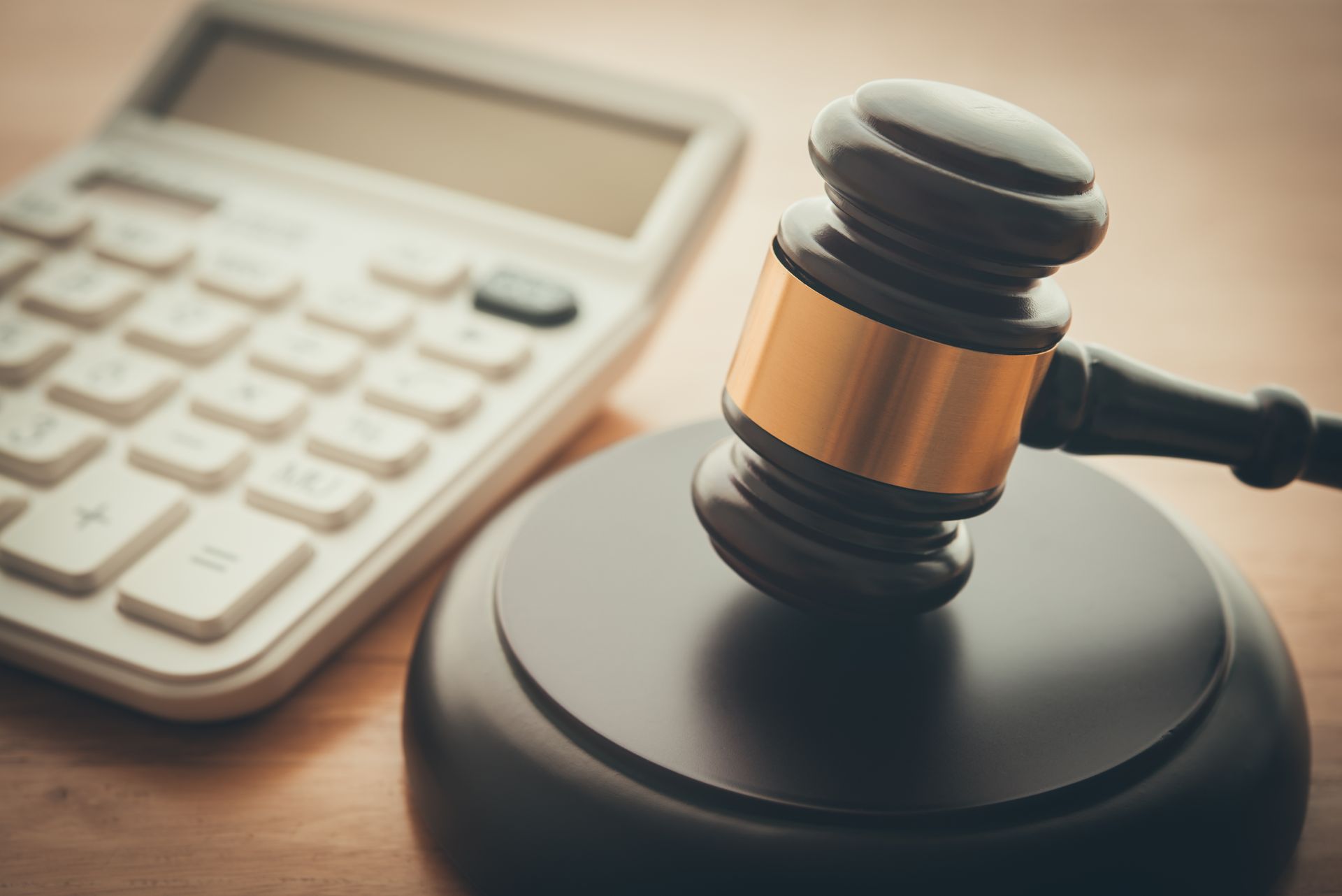 Wooden judge's gavel with a brass band on a sound block beside a white calculator on a desk.
