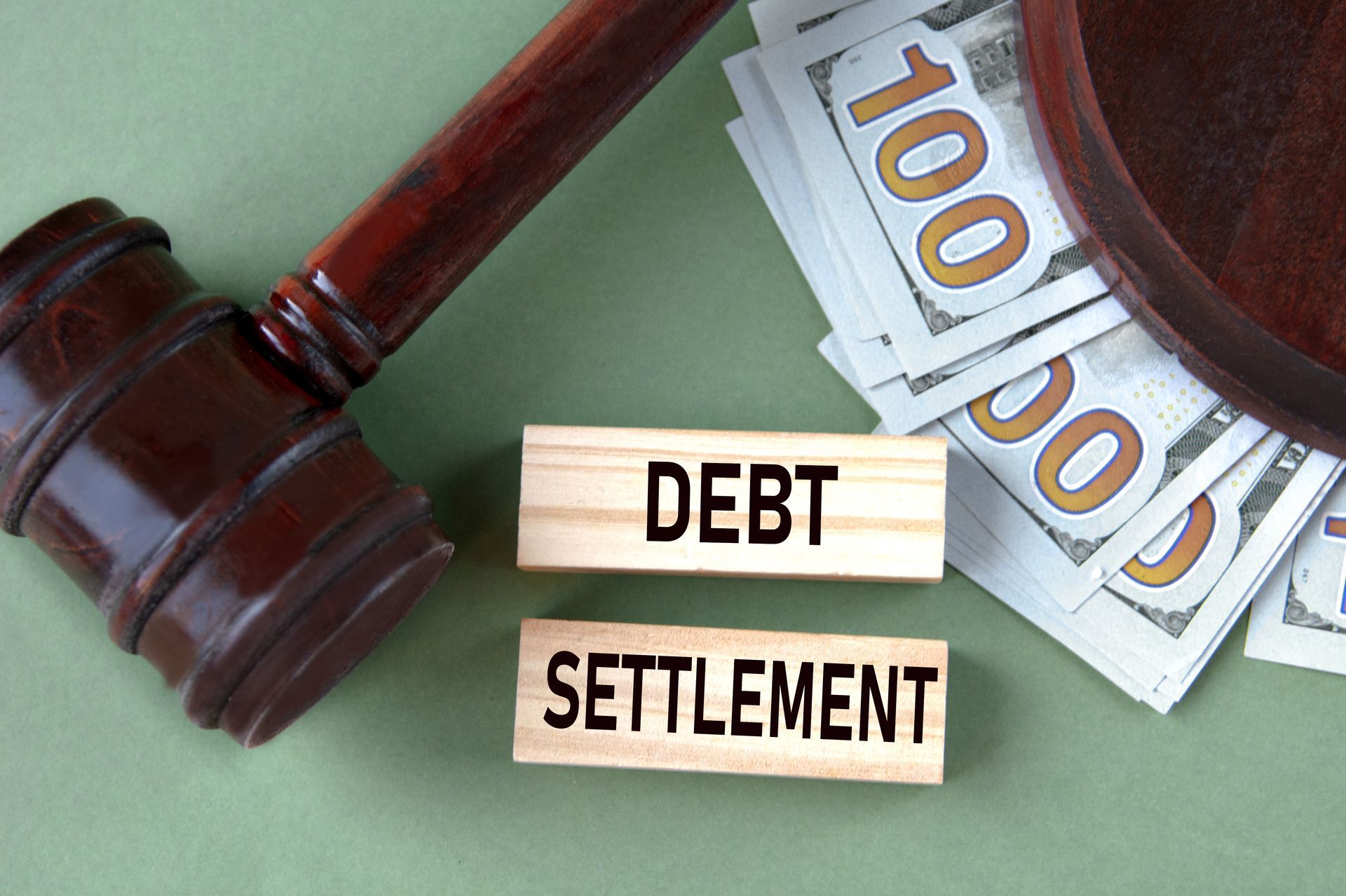 The words “DEBT SETTLEMENT” on wooden blocks beside a judge's gavel and dollar banknotes. The words “DEBT SETTLEMENT” on wooden blocks beside a judge's gavel and dollar banknotes.