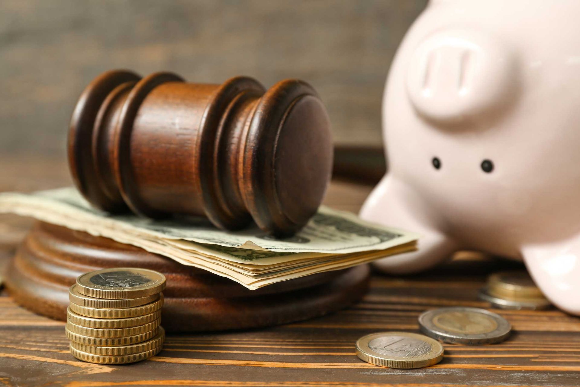 Piggy bank with judge gavel and money on brown wooden background.