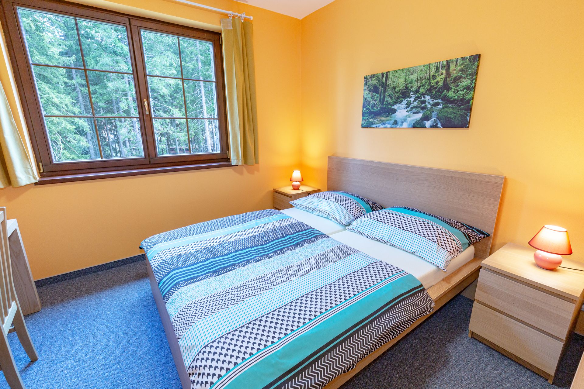 Spálňa s posteľou, nočným stolíkom, lampami a obrazom na stene.