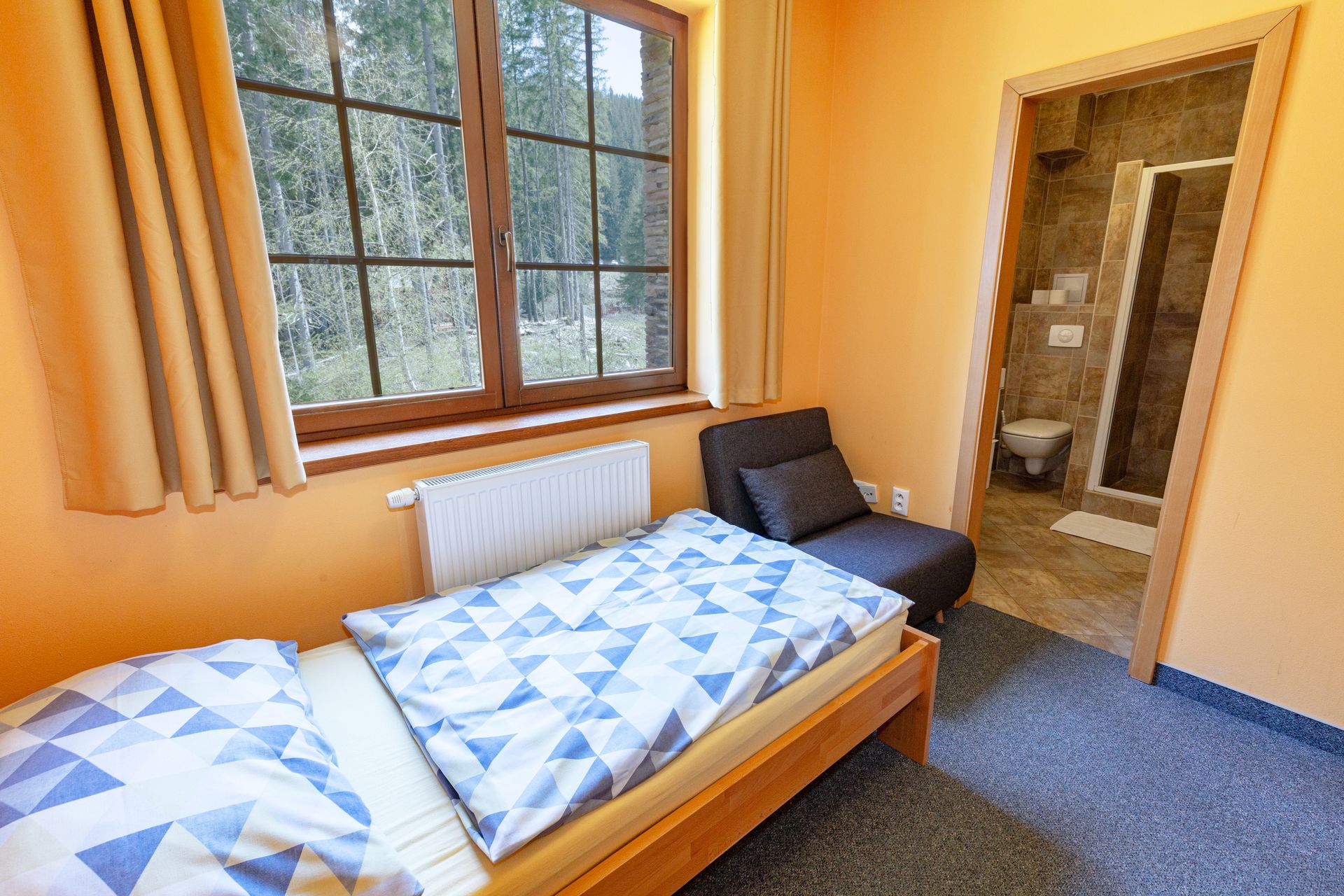 Spálňa s dvoma posteľami, kreslom a oknom.