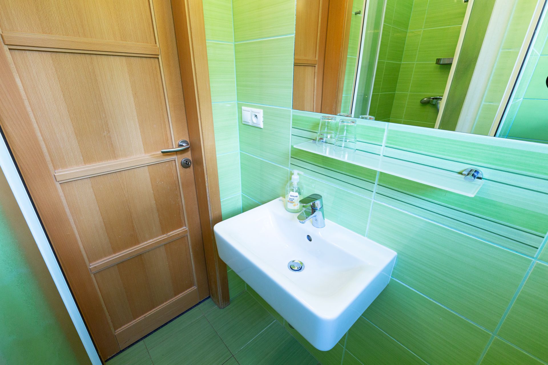 Kúpeľňa so zelenými dlaždicami, umývadlom a zrkadlom