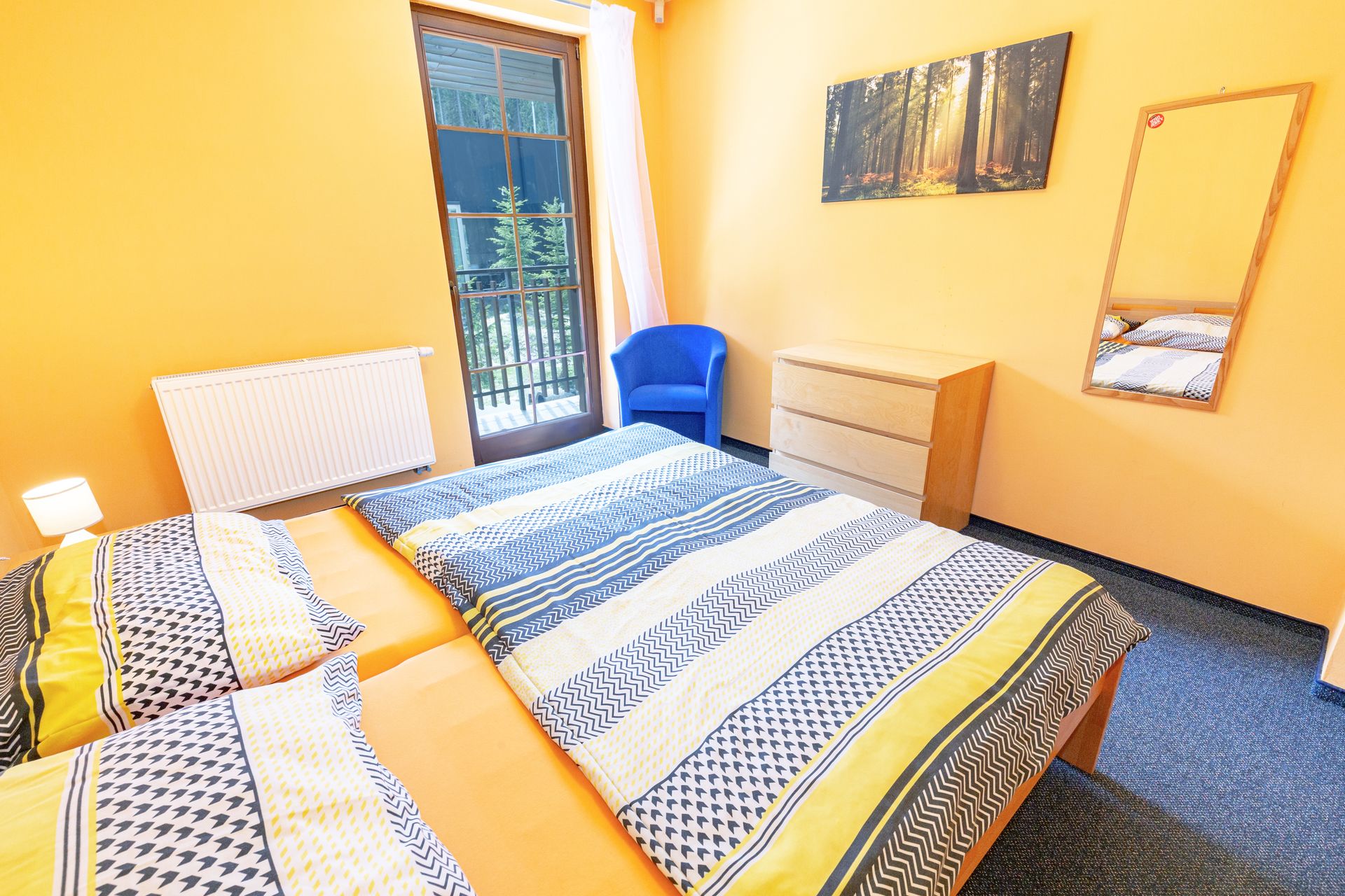 Spálňa s dvoma posteľami, modrým kreslom, komodou a zrkadlom.