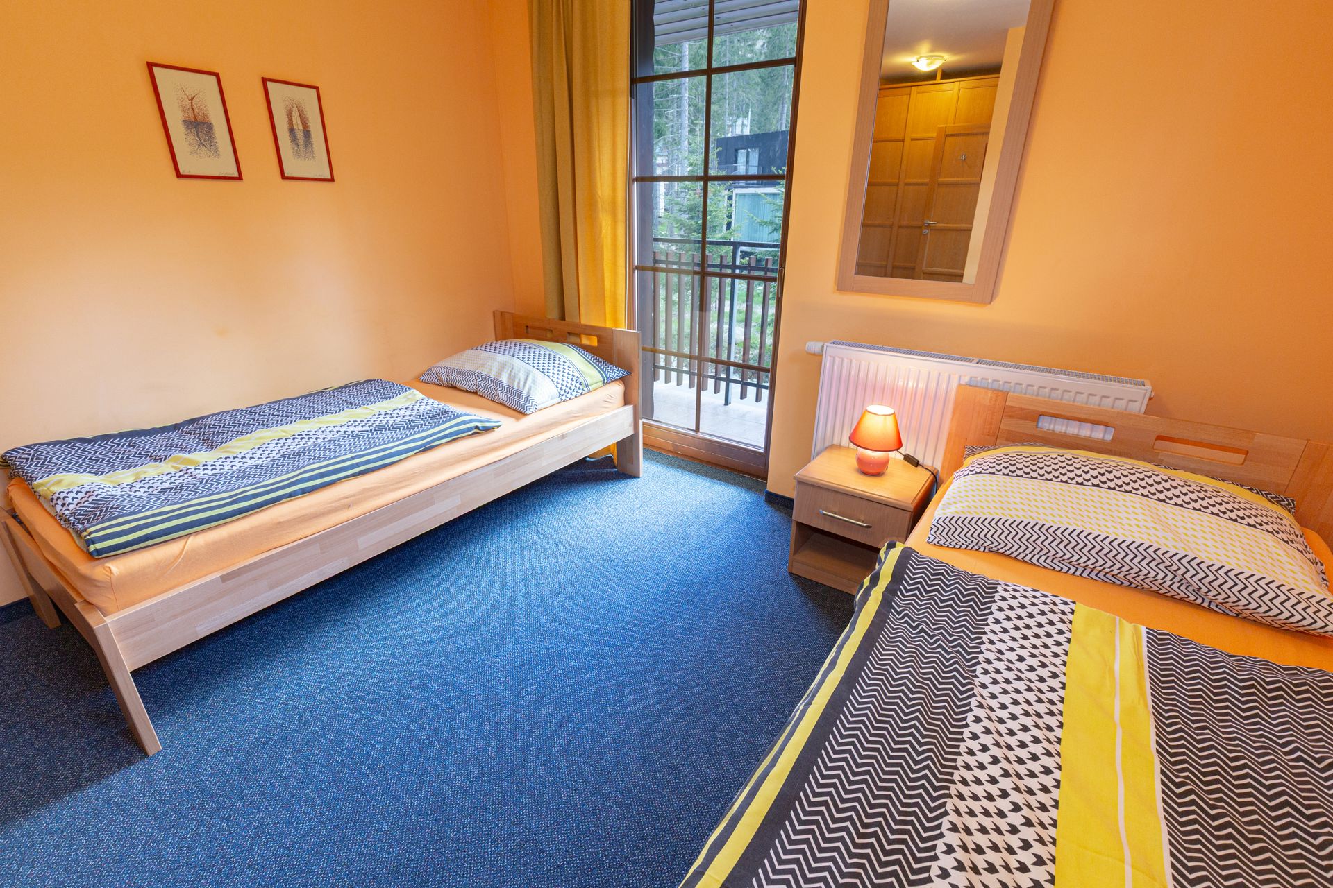 Spálňa s dvoma posteľami, nočným stolíkom, zrkadlom a balkónom.