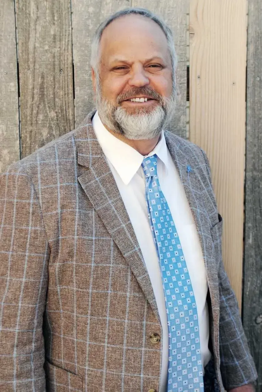 A man in a suit and tie is standing in front of a wooden fence.