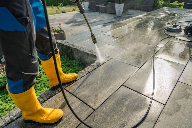A man is cleaning a driveway with a high pressure washer.