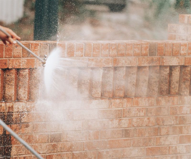 Pressure washing a red brick wall. Water spraying, creating mist.