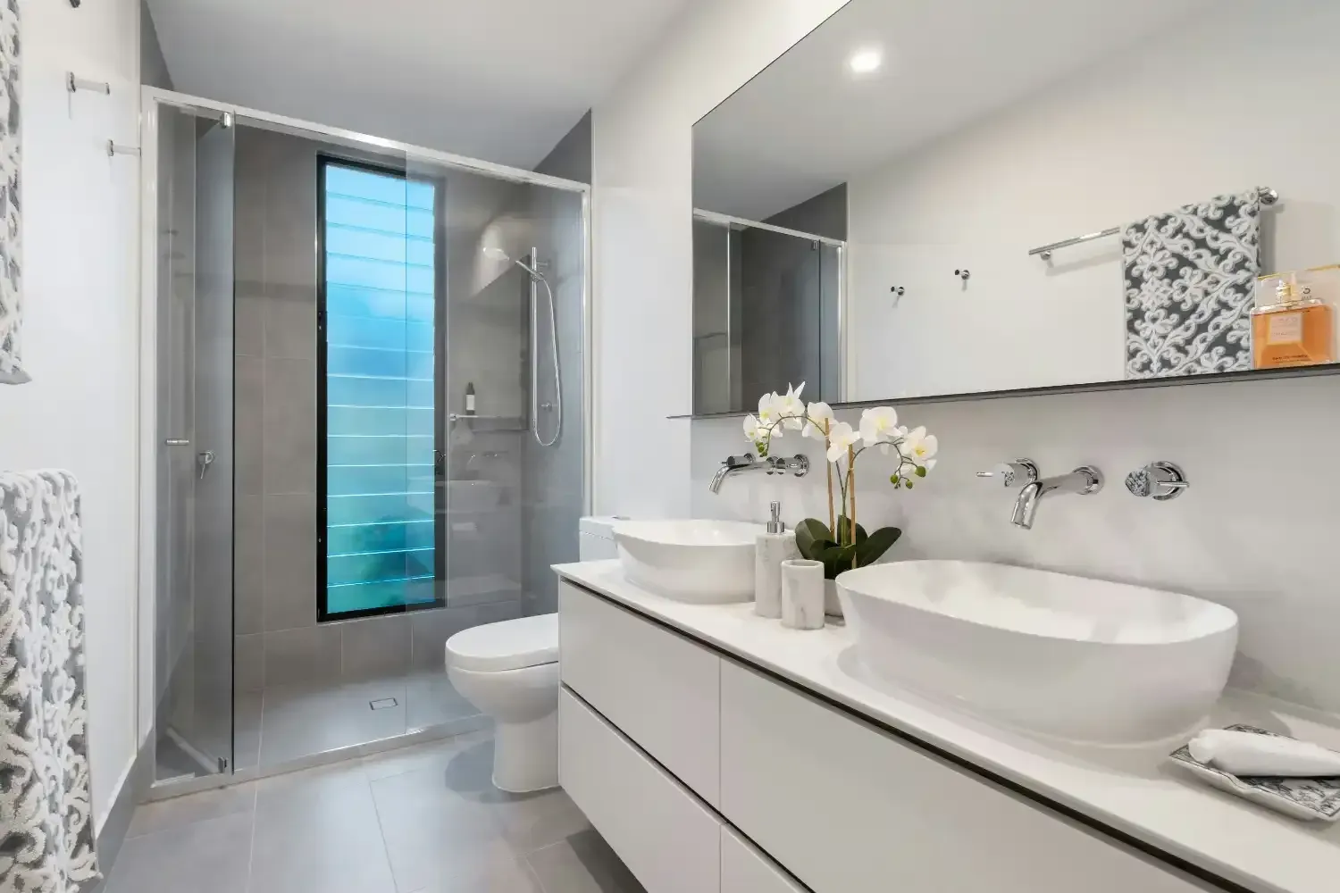Modern white bathroom with glass shower, large mirror, and double sink vanity