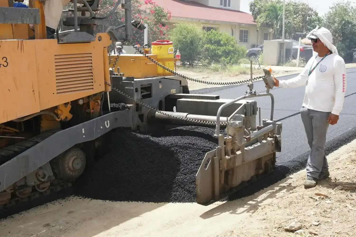 Road crew operating a paving machine to lay fresh black asphalt on a street