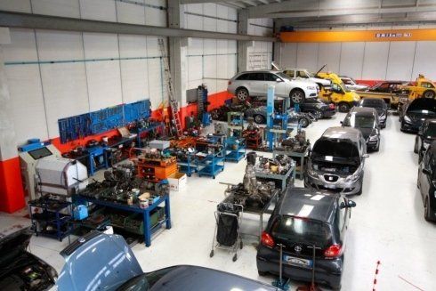Automotive workshop with several cars and engines under repair, tools and equipment throughout the garage