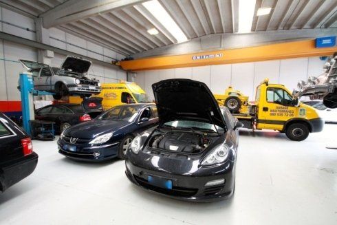 Car showroom with several cars, including a black car with its hood open and a yellow tow truck.