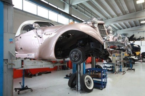 Classic pink car body on a lift in an auto workshop, with tools and another vehicle in the background