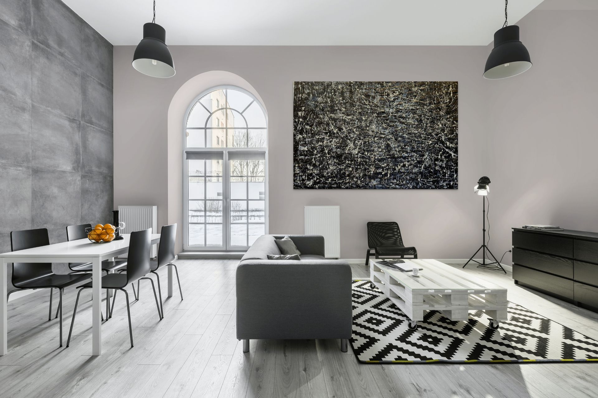 A modern living and dining room with gray walls, a pallet coffee table, geometric rug, and a large abstract painting.