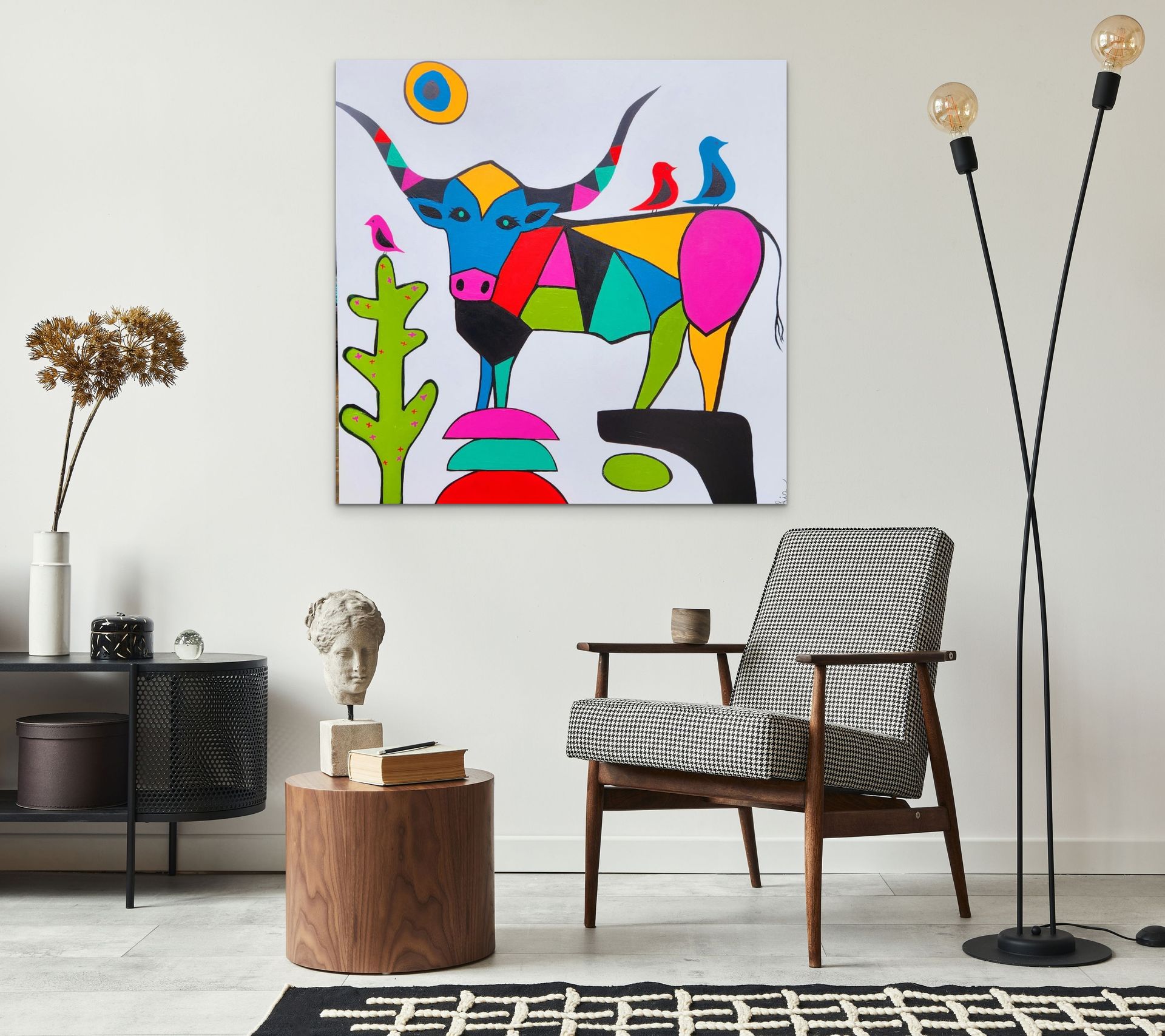 A colorful, geometric bull painting hangs above an armchair in a modern, minimalist living room.