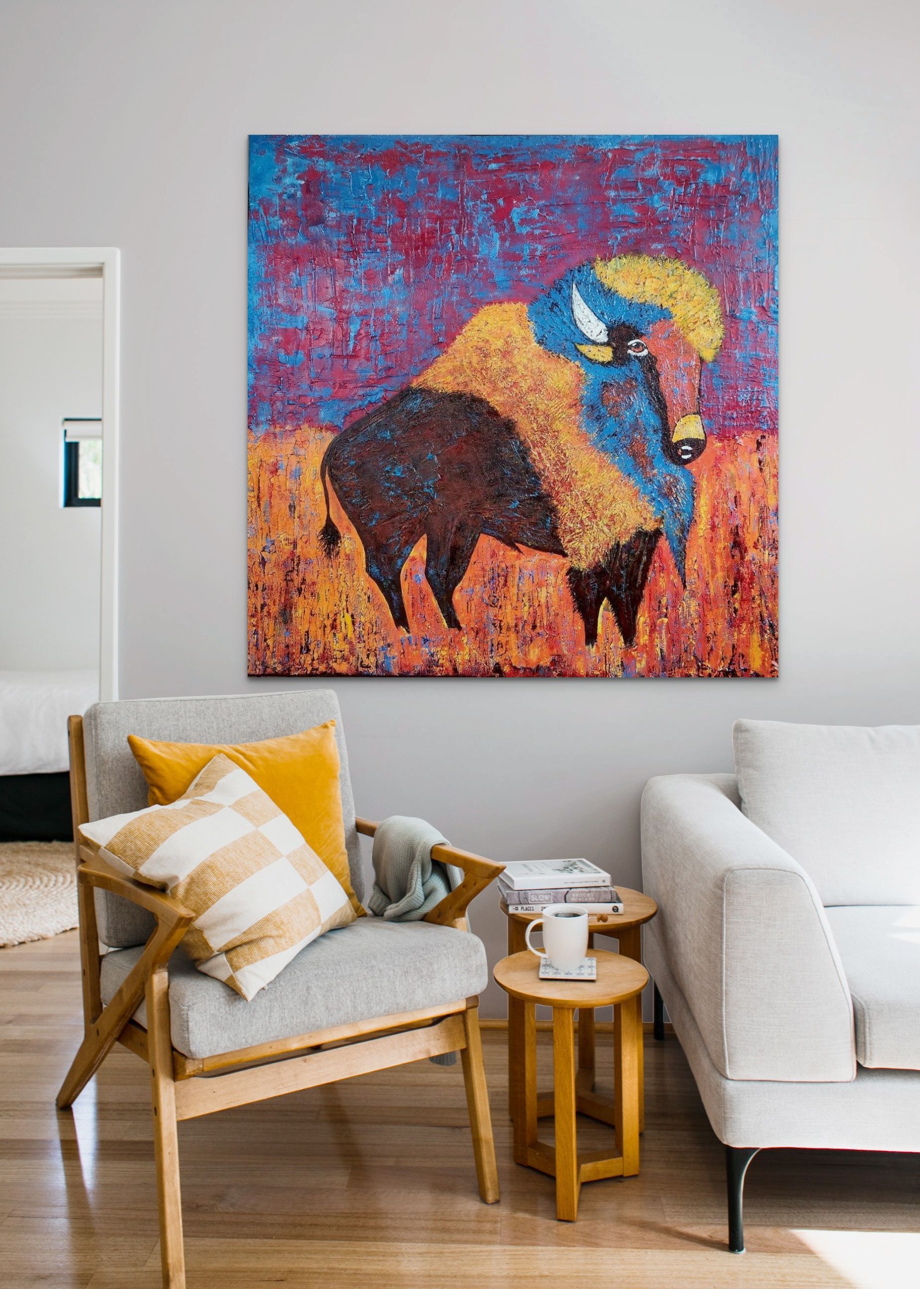A painting of a bison hangs above a cozy living room nook featuring a grey armchair, mustard pillows, and side tables.