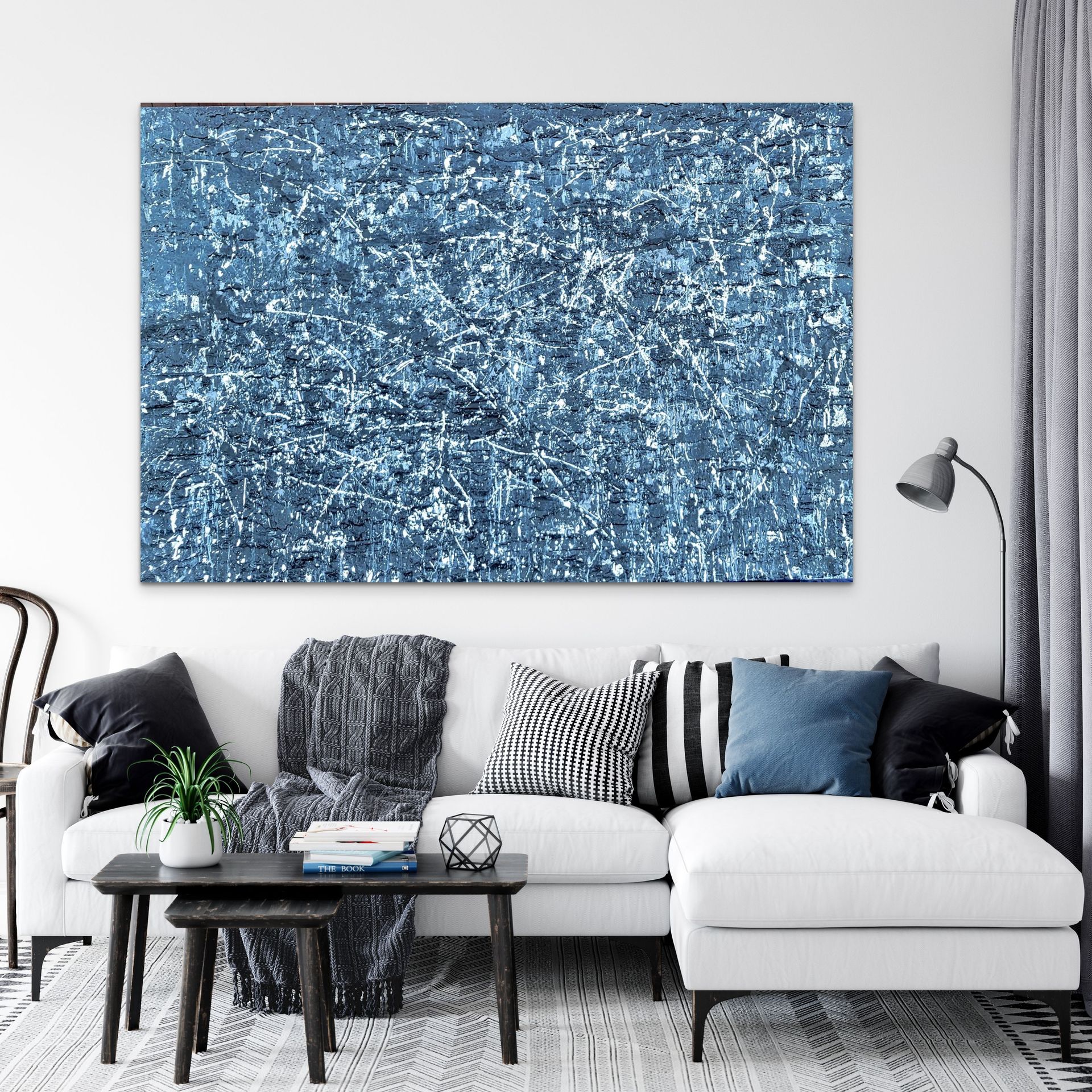 A white sofa with patterned pillows sits before a large, blue abstract painting in a modern living room.