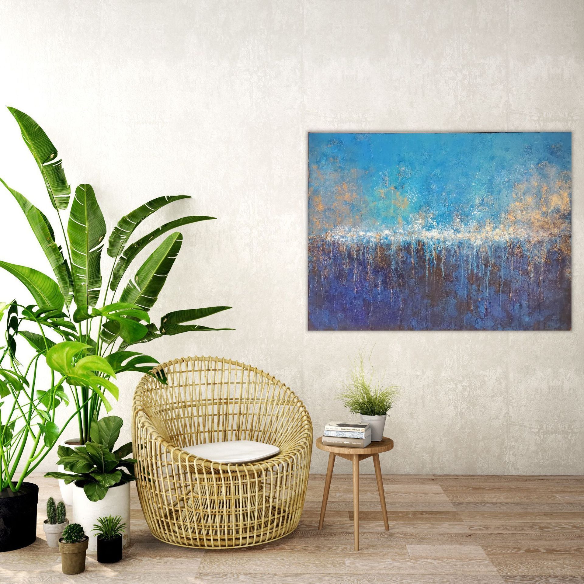 A blue abstract painting hangs above a rattan chair, a small side table with books, and potted plants in a modern room.