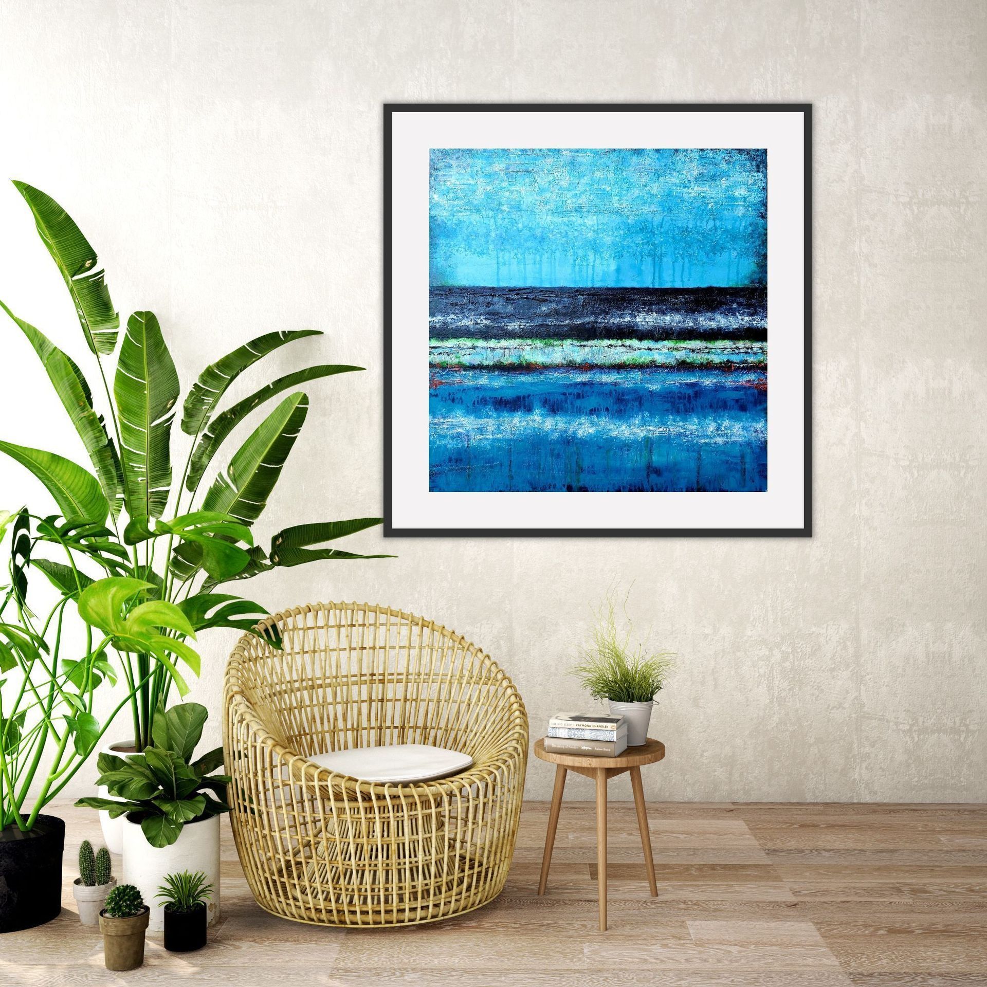 A framed square abstract blue painting hangs above a rattan chair, a small side table, and several potted houseplants.