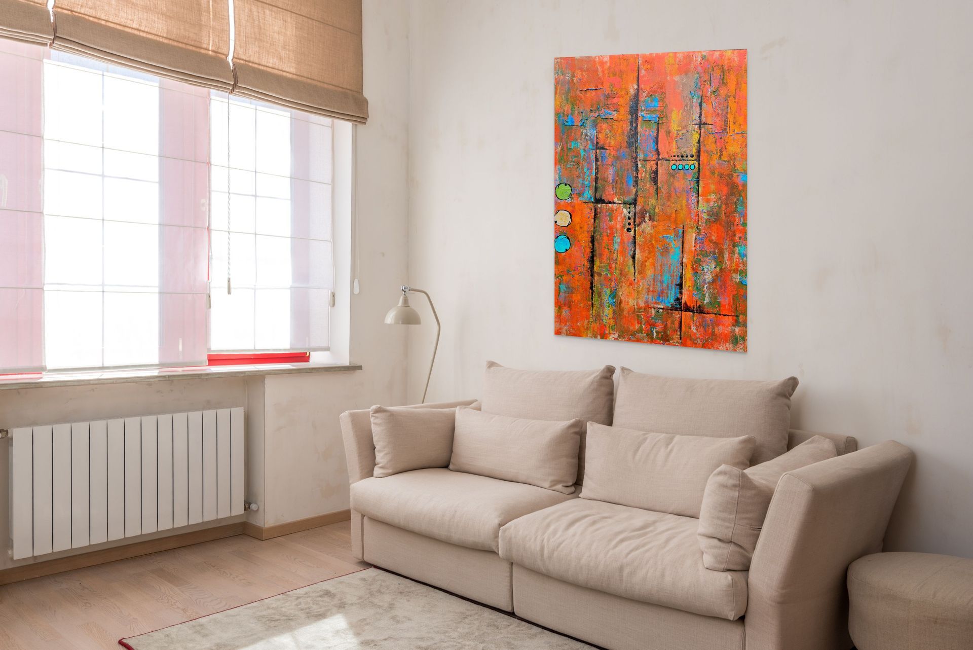 A colorful, textured abstract painting hangs on a beige wall above a white sofa and a wooden side table with a lamp.