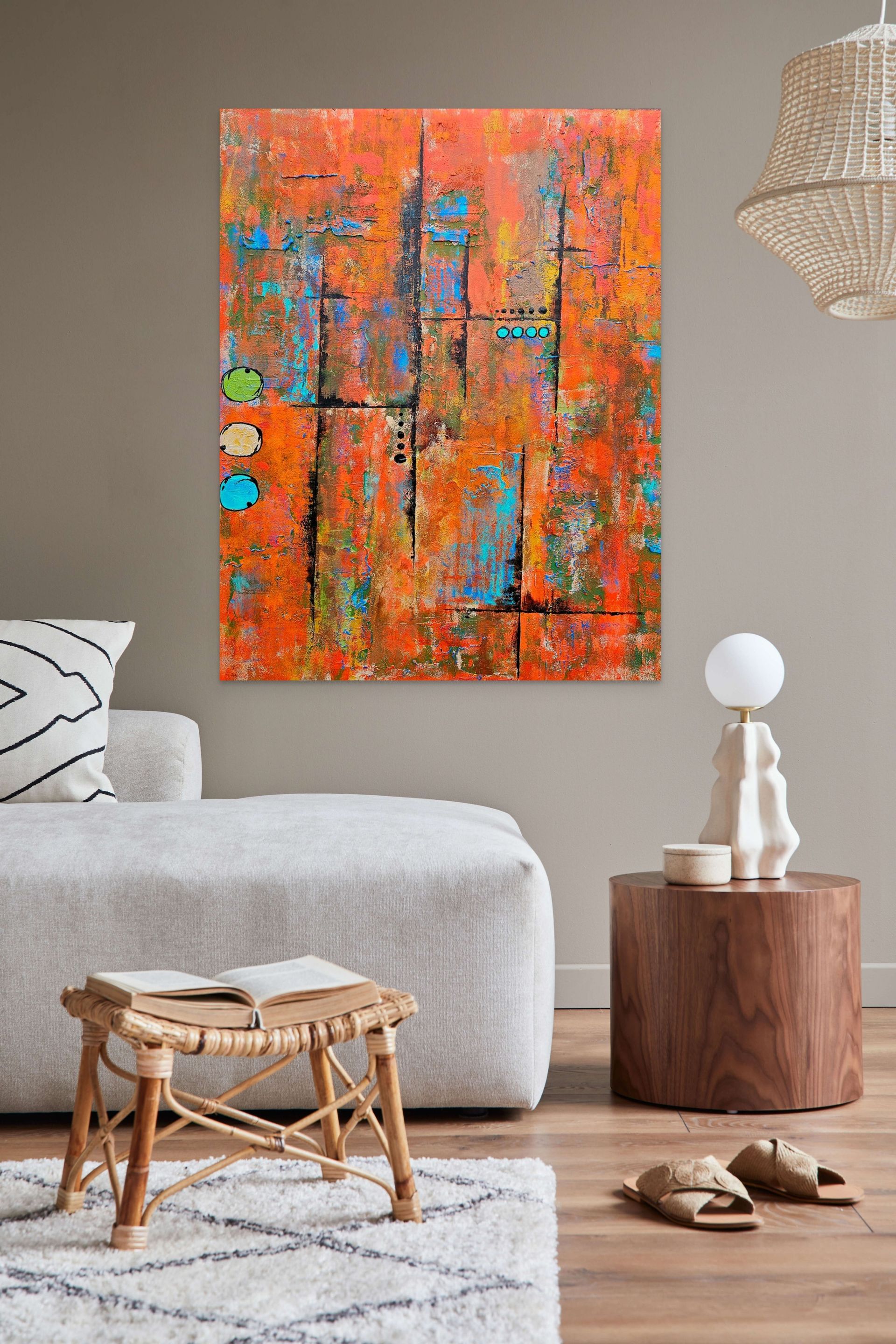 A colorful, textured abstract painting hangs on a beige wall above a white sofa and a wooden side table with a lamp.