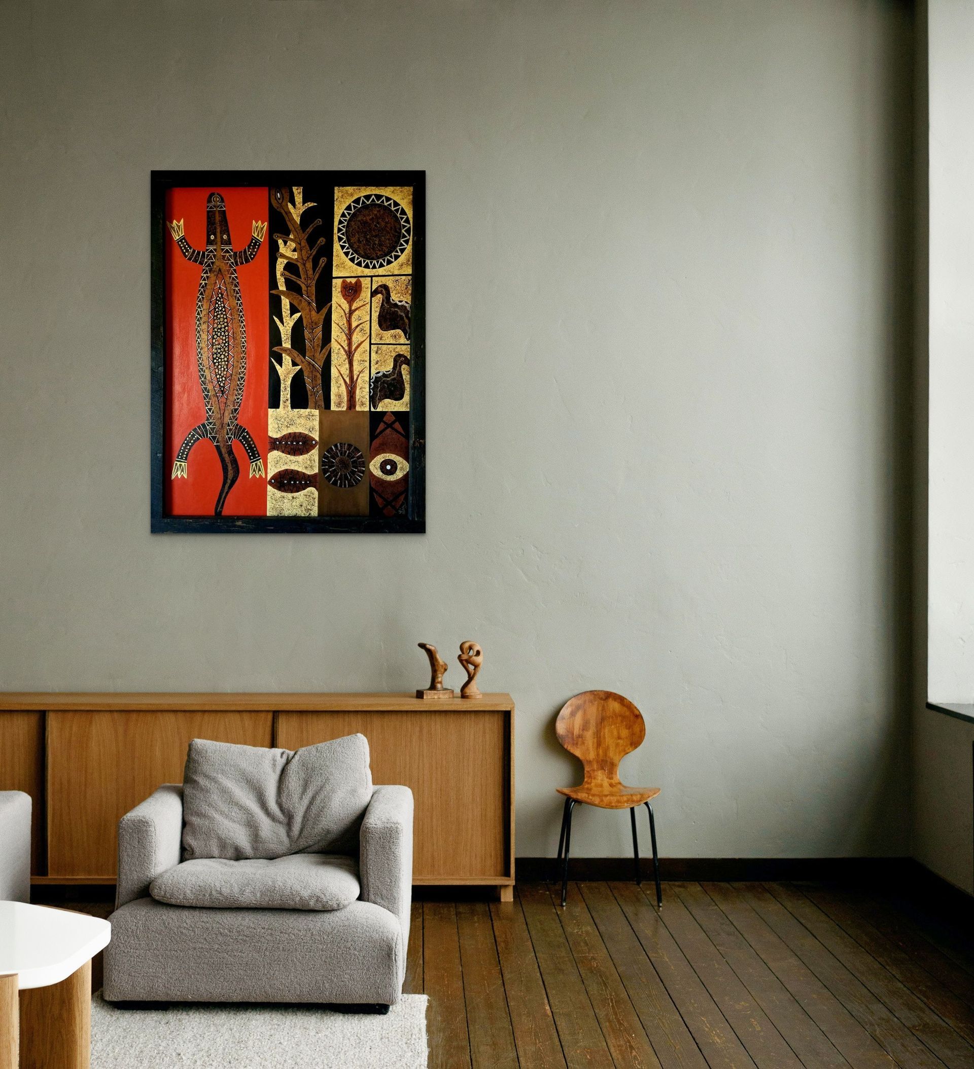 A modern living room features a wooden cabinet, a grey armchair, a small wooden chair, and framed ethnic art on the wall.