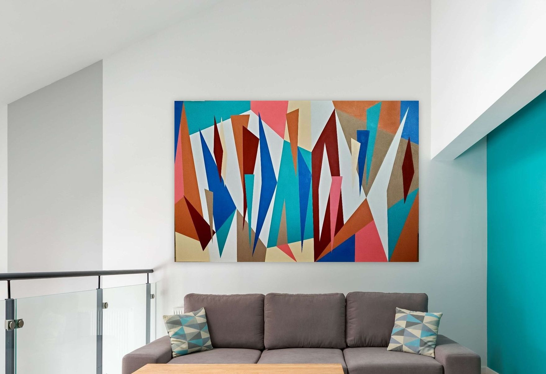 A large, geometric abstract painting with colorful triangles hanging above a gray sofa in a brightly lit room.