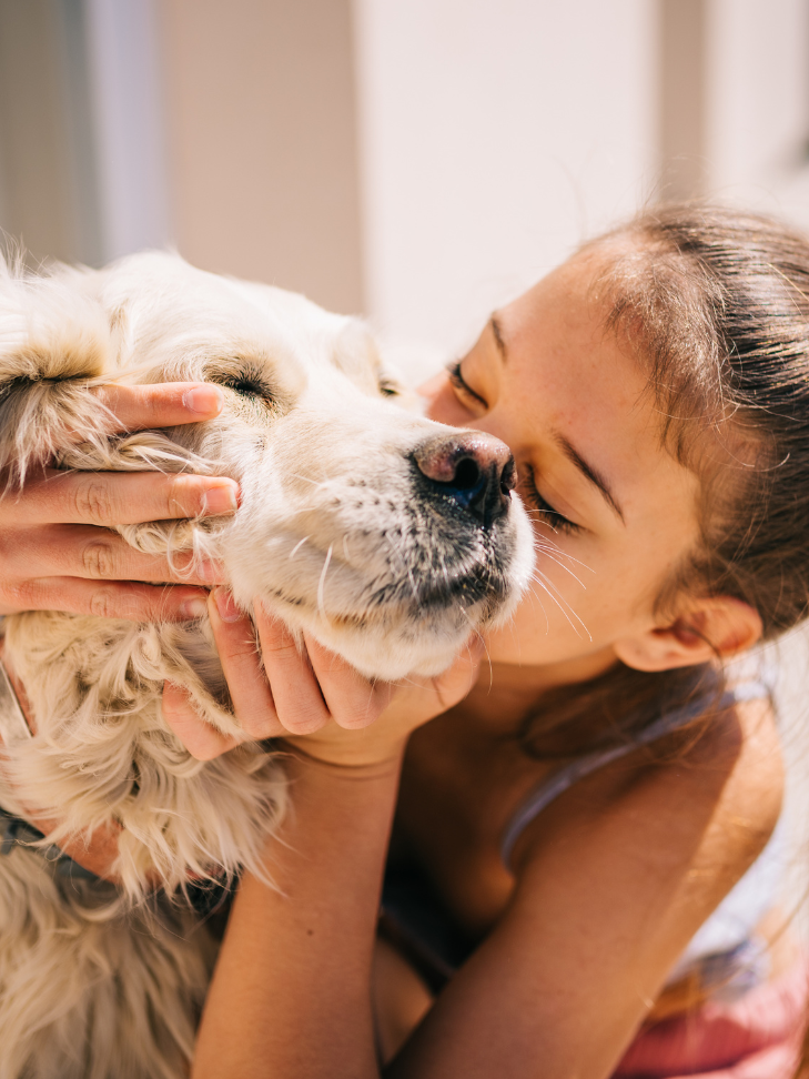 A girl is kissing a dog on the nose.