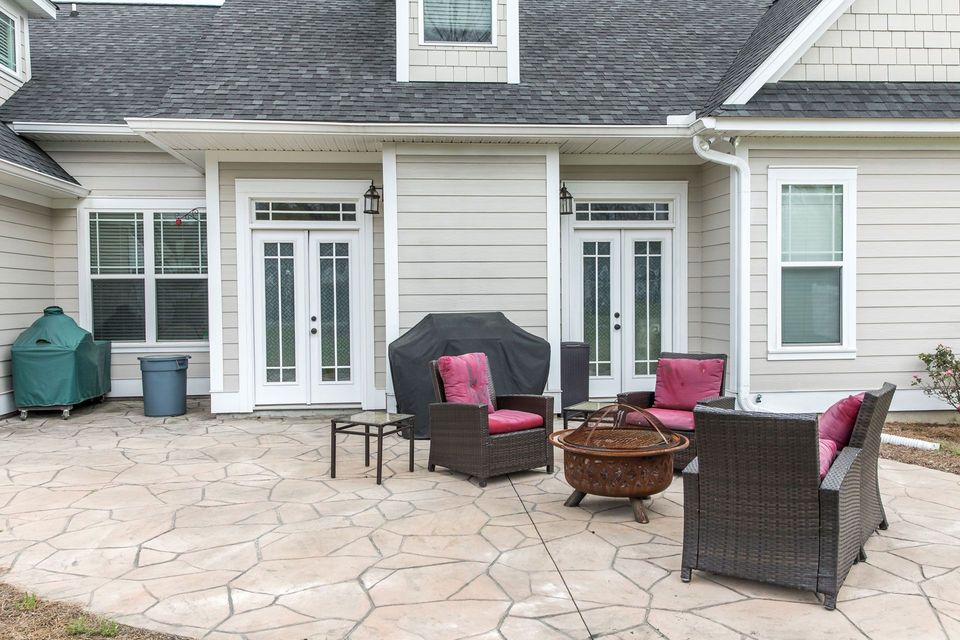 A patio with stone pavers, wicker outdoor furniture with red cushions, a fire pit, and a grill in front of a house.