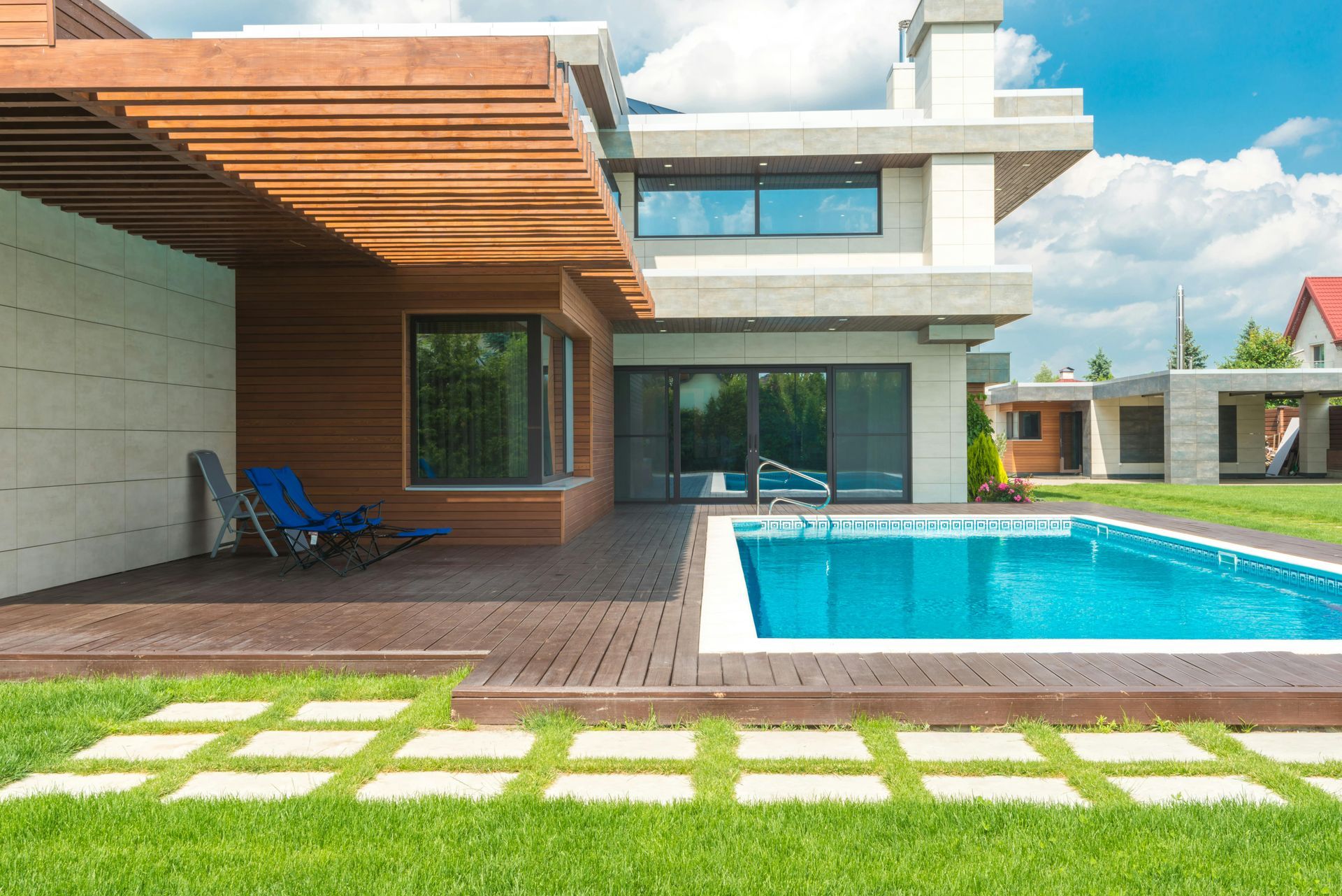 A modern house with a wooden slatted roof, a pool deck, and a turquoise swimming pool on a sunny day.