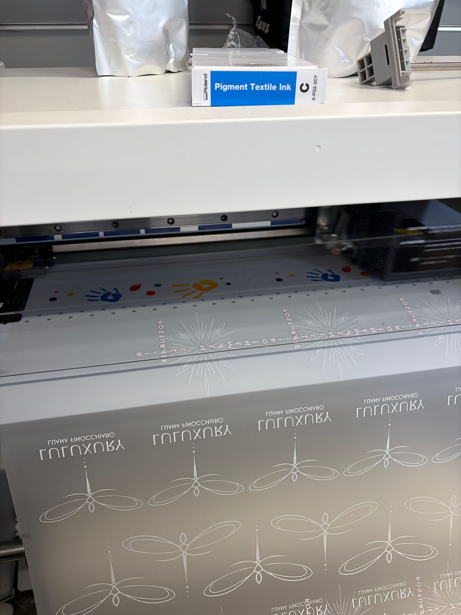 Una stampante 3D in un'officina, intenta a stampare un foglio grigio con un motivo a rilievo sotto la testina di stampa.
