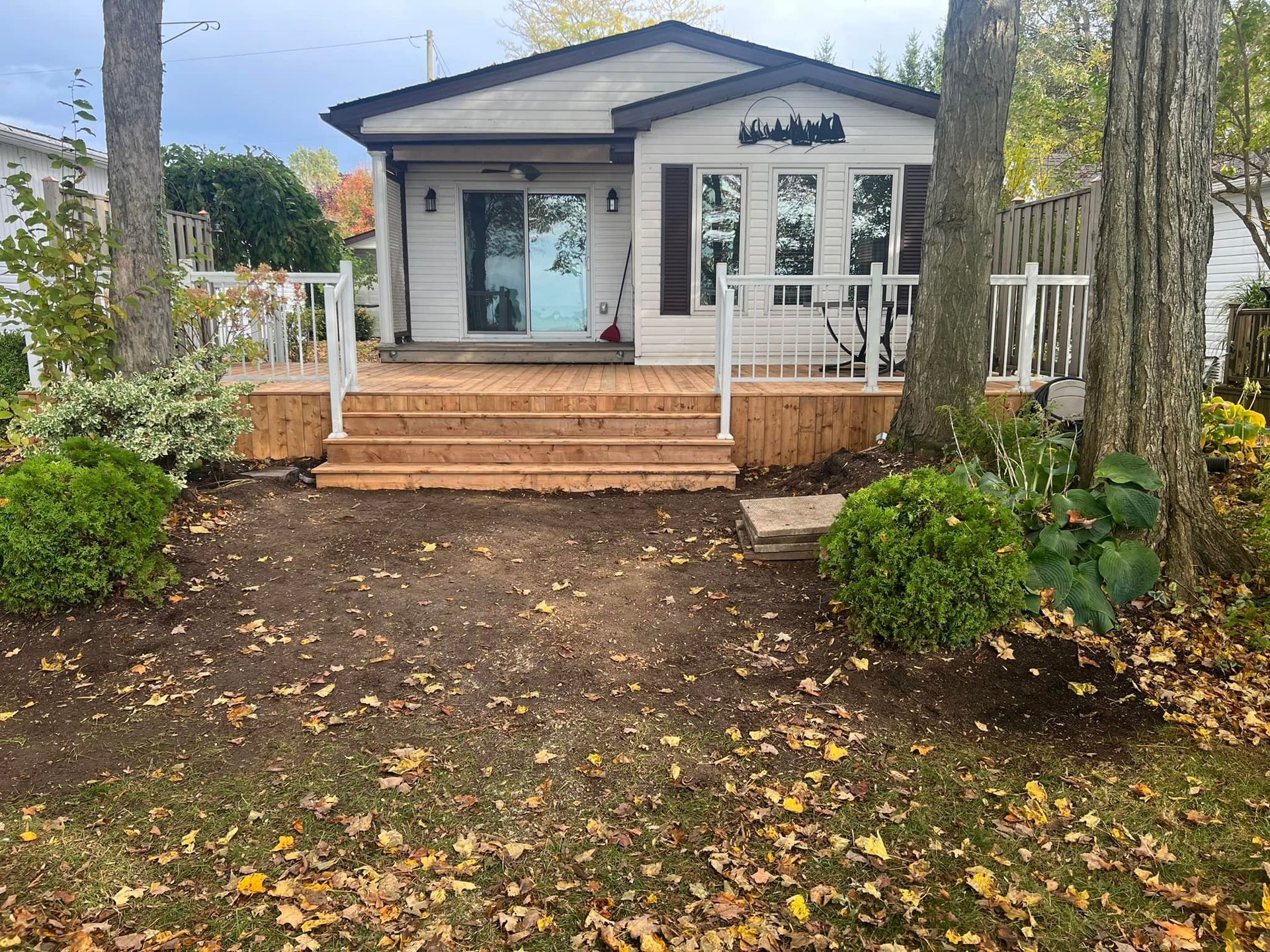 A small white house with a wooden deck and stairs surrounded by trees.