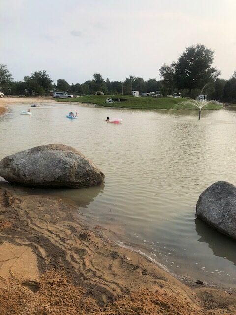 Small pond with swimmers, large rocks in the foreground, and fountains spraying water in the distance.