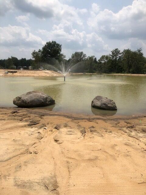 Sandy pond with two rocks in the foreground and a fountain spraying water under a cloudy sky